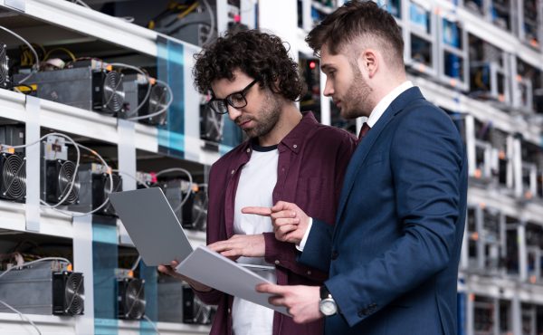 businessman and computer engineer working with laptop together at bitcoin mining farm