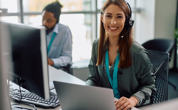 Happy customer service representative working at call center office and looking at camera.